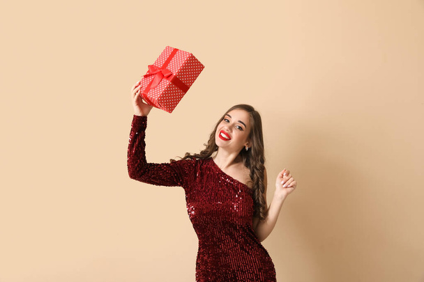 Young woman with gift on beige background. New Year celebration - Photo, Image