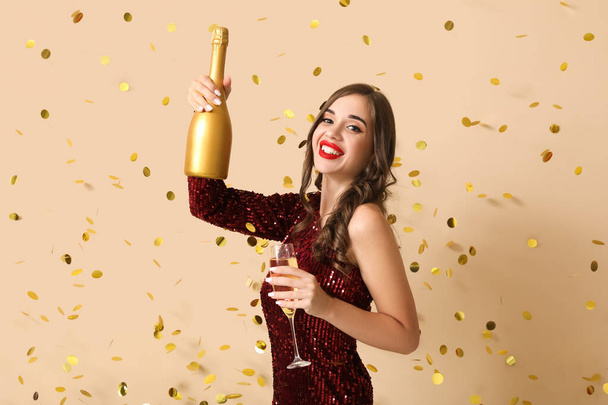Junge Frau mit Champagner und fallendem Konfetti auf beigem Hintergrund. Neujahrsfeier - Foto, Bild