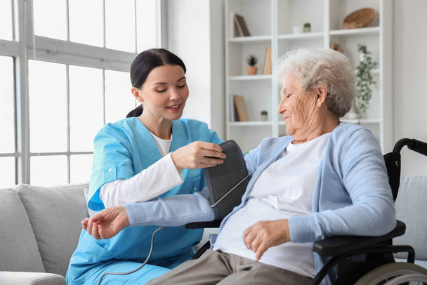 Žena zdravotní sestra měření krevního tlaku starší ženy na invalidním vozíku doma - Fotografie, Obrázek