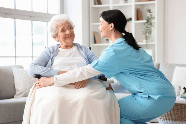 Female nurse caring about senior woman in wheelchair at home - Photo, Image