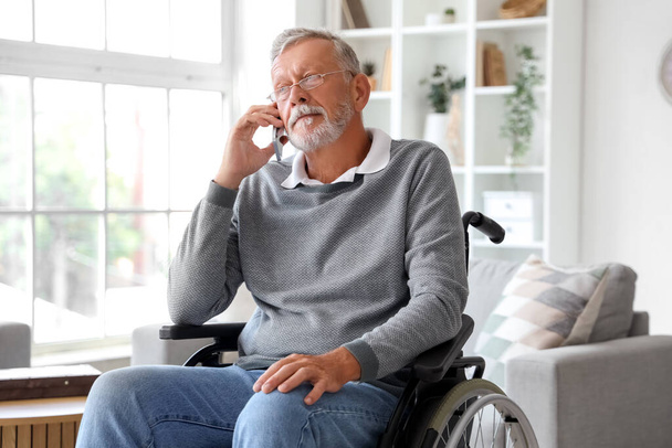 Idősebb férfi tolószékben beszél mobiltelefonnal otthon - Fotó, kép