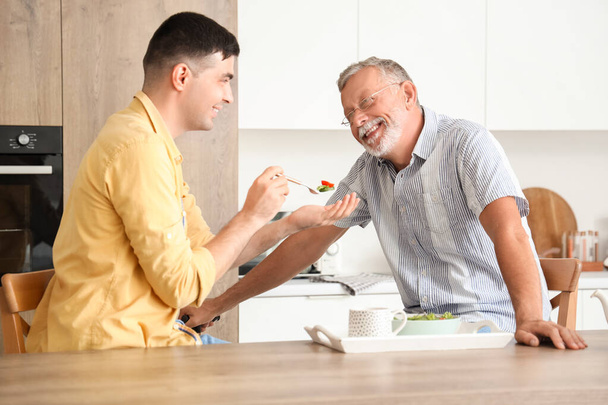 Young man feeding his father in kitchen - Photo, Image