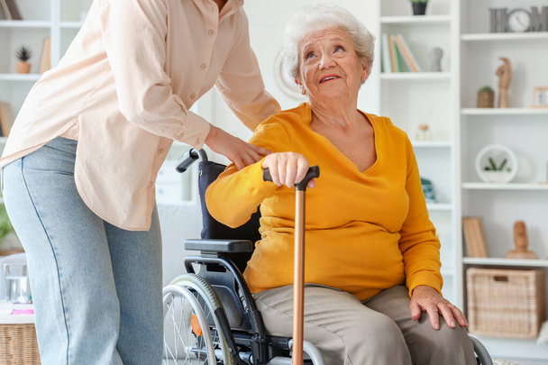 Ηλικιωμένη γυναίκα σε αναπηρική καρέκλα με ραβδί και η κόρη της στο σπίτι - Φωτογραφία, εικόνα