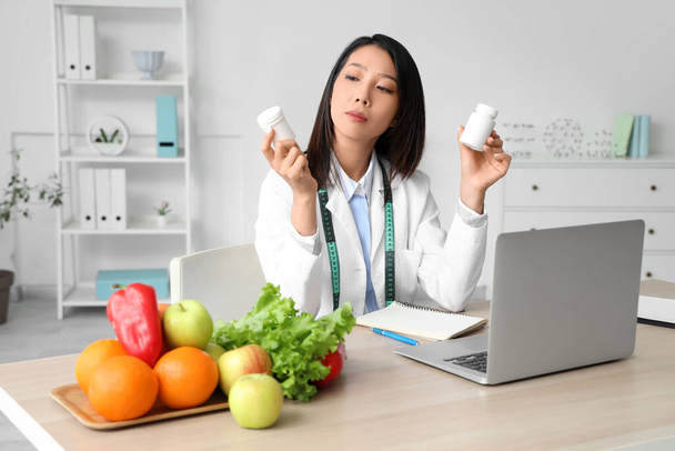 Asiatische Ernährungsberaterin mit Tablettenflaschen am Tisch im Büro - Foto, Bild