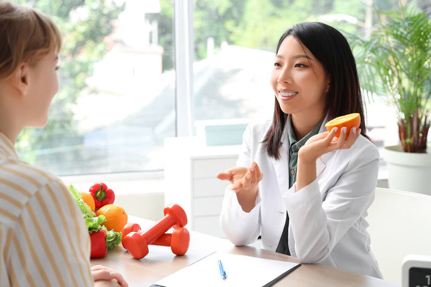 Vrouwelijke Aziatische voedingsdeskundige met oranje en patiënt in functie - Foto, afbeelding