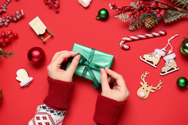 Руки женщины с рождественским подарком и красивые украшения на красном фоне, крупным планом - Фото, изображение