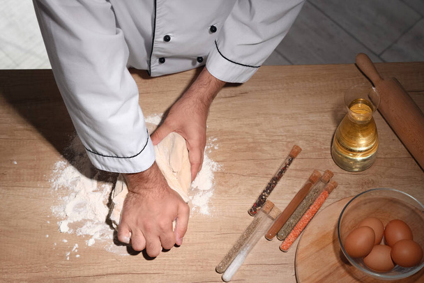 Jonge chef deeg kneden op tafel in de bakkerij - Foto, afbeelding