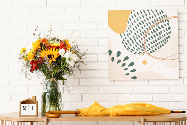 Полка с букетом осенних цветов и зонтиком возле белой кирпичной стены - Фото, изображение