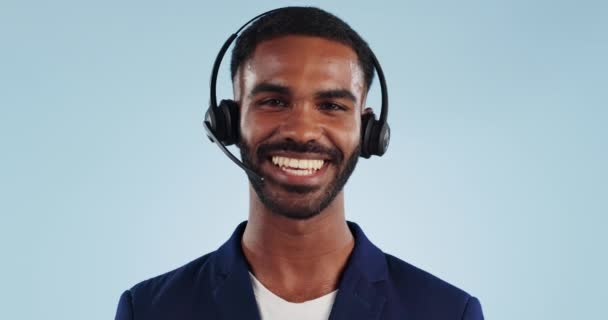Telemarketing, ακουστικά και το πρόσωπο του μαύρου άνδρα στο στούντιο μιλώντας με χαμόγελο, βοήθεια και συμβουλές. Τηλέφωνο κλήση, συζήτηση και ευτυχής σύμβουλος crm, υποστήριξη πελατών ή πράκτορα callcenter σε μπλε φόντο - Πλάνα, βίντεο