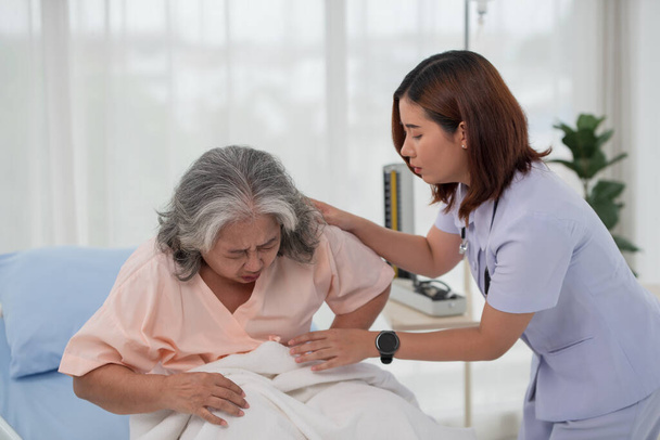 Infirmière asiatique aidant une patiente asiatique âgée souffrant de maux d'estomac sur un lit dans une salle d'hôpital avec diagnostic ou traitement, traitant une femme âgée - Photo, image
