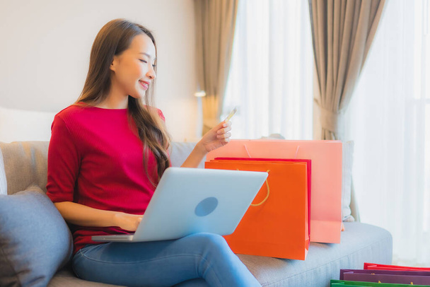 Porträt schöne junge asiatische Frau verwenden Laptop-Computer mit Kreditkarte für Online-Shopping mit Tasche auf dem Sofa - Foto, Bild