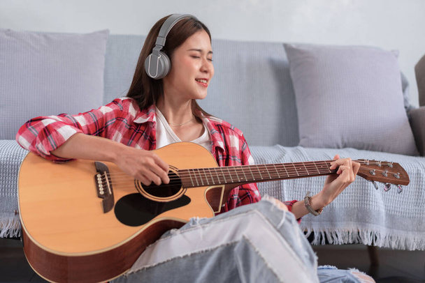 Hobby concept, Young asian woman wearing headphone and sit on the floor to playing acoustic guitar. - Foto, imagen