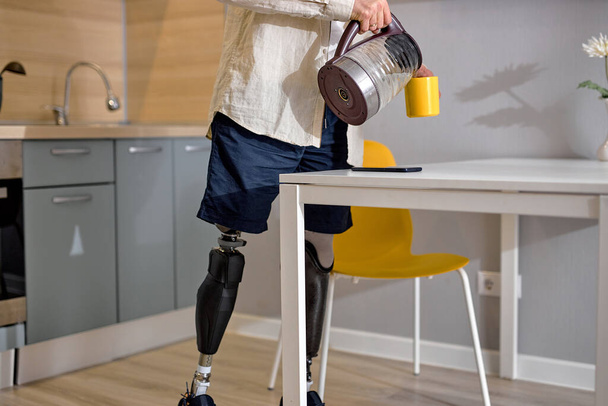 deficiente ou deficiente com deficiência em pé sobre prótese inteligente biônica na cozinha, fazendo café ou chá para si mesmo em casa. dentro de casa. de manhã. estilo de vida deficiência - Foto, Imagem