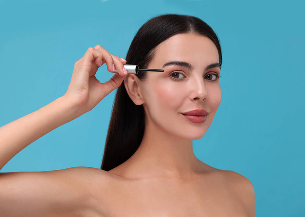 Beautiful woman applying serum onto her eyelashes on light blue background. Cosmetic product - Foto, Imagem