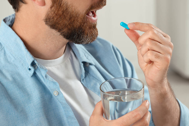 Hombre con vaso de agua tomando píldora sobre fondo borroso, primer plano - Foto, Imagen