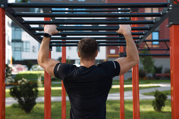 Man training on monkey bars at outdoor gym, back view - Фото, зображення