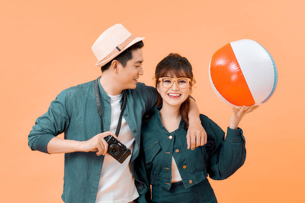 Молодая привлекательная пара с надувным мячом и камерой на желтом фоне - Фото, изображение