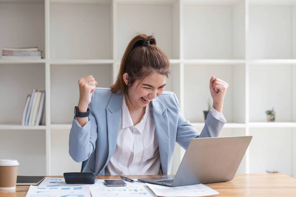 Ασιάτισσες επιχειρηματίες δείχνουν χαρούμενη έκφραση της επιτυχίας στη δουλειά χαμογελώντας χαρούμενα με έναν φορητό υπολογιστή σε ένα σύγχρονο γραφείο.. - Φωτογραφία, εικόνα