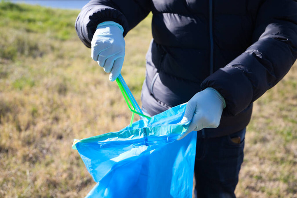 Ormandan plastik çubukları alıp plastik torbaya koyan bir gönüllü elinin ayrıntıları. Dünya Günü ve Dünya Çevre Günü kavramı 5 Haziran. - Fotoğraf, Görsel