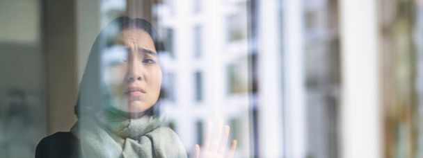 Az ázsiai nő rosszul érzi magát, otthon marad, féltékeny, szomorú arccal néz ki az ablakon, ki akar menni, de megfázik.. - Fotó, kép