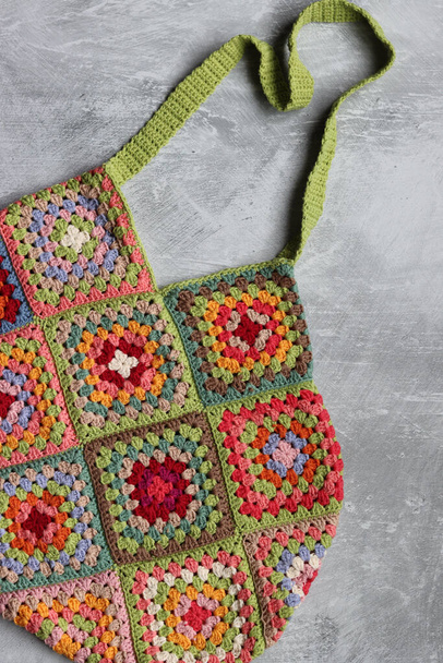 Handmade reusable shopping bag made of crocheted granny squares. Colorful grocery bag close up photo. Sustainable lifestyle concept. Grey background with copy space.  - Photo, Image