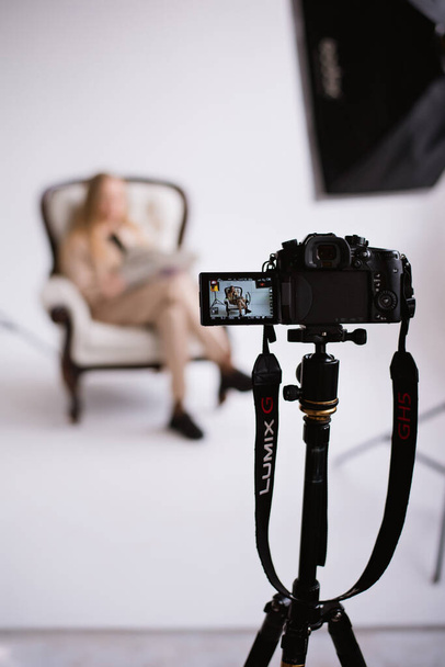 Женщина-блогер, блондинка с камерой на штативе в студии. Ношение формального обнаженного брючного костюма на белом изолированном фоне, обезображивание человека - Фото, изображение