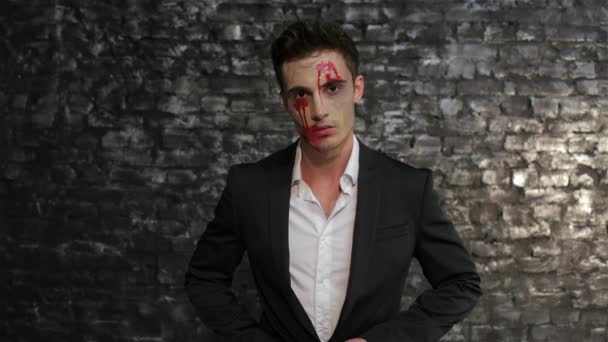 Male vampire wipes away the blood from his mouth. Man in the image of the vampire posing on black background of a brick wall. Halloween concepts and costumes - Footage, Video