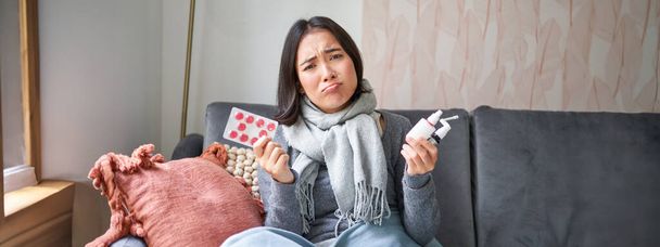 Korean woman showing medical pills, sore throat sprays, feeling sick, staying at home as feeling unwell, catching cold in winter. - Photo, Image