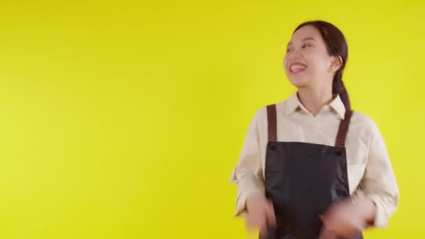 Portré fiatal ázsiai barista nő visel kötény bemutató és hüvelykujj fel a sárga háttér, pincérnő vagy vállalkozó vidám és mutat valamit, kisvállalkozás vagy startup, pincér kávézó. - Felvétel, videó