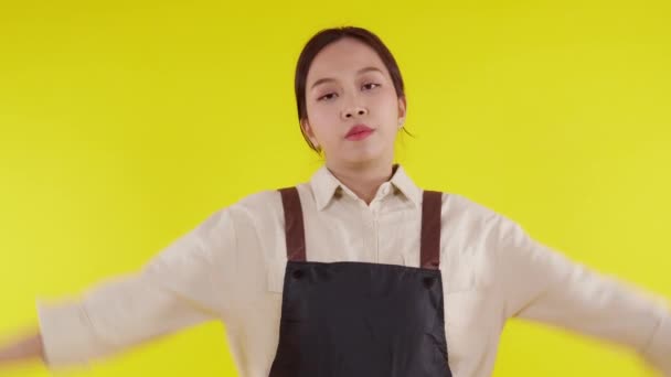 Portré fiatal ázsiai barista nő visel kötény álló és boldogtalan gesztus nem tetszik a sárga háttér, pincérnő vagy vállalkozó csalódott, kisvállalkozás vagy startup kudarccal. - Felvétel, videó