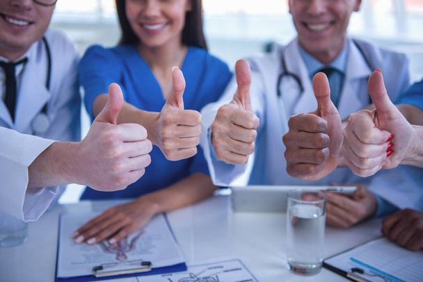 Bijgesneden afbeelding van succesvolle artsen tonen duimen en glimlachen tijdens de vergadering op de conferentie - Foto, afbeelding