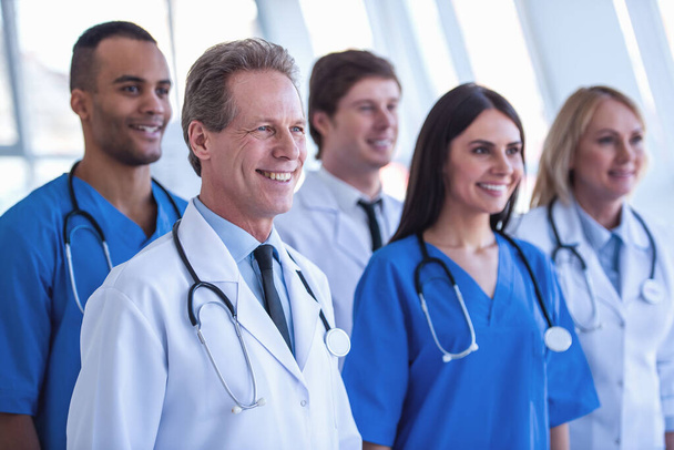 Equipo exitoso de médicos están mirando hacia adelante y sonriendo mientras están de pie en el hospital
 - Foto, imagen