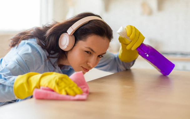 Młoda gospodyni domowa w gumowych rękawiczkach sprzątanie stół jadalny w kuchni, pokojówka utrzymanie jej domu schludny i czysty, wycieranie powierzchni z mikrofibry tkaniny - Zdjęcie, obraz