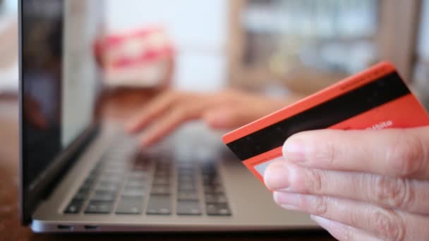 サイドビュー。 オンラインでクレジットカードで購入する若い女性の手. ラップトップを使用して自宅でオンライン取引を行う女性. - 映像、動画