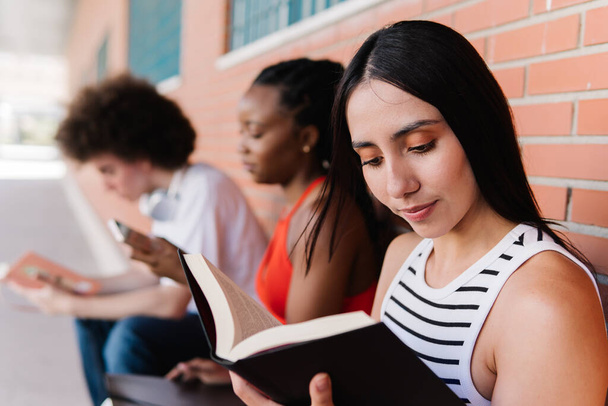 Три багатоетнічні групи студентів, які читають і використовують телефон, сидячи в кампусі - Фото, зображення