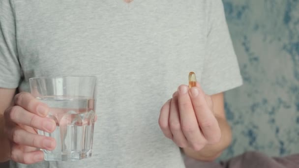 Homem bebendo cápsula com ômega 3, vitamina D com copo de água. Suplemento nutricional com óleo de peixe. Conceito de suporte e tratamento em saúde. - Filmagem, Vídeo