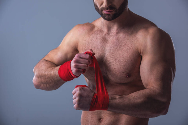 Imagen recortada de un hombre musculoso guapo con las manos vendadas del torso desnudo antes del boxeo, sobre fondo gris
 - Foto, Imagen