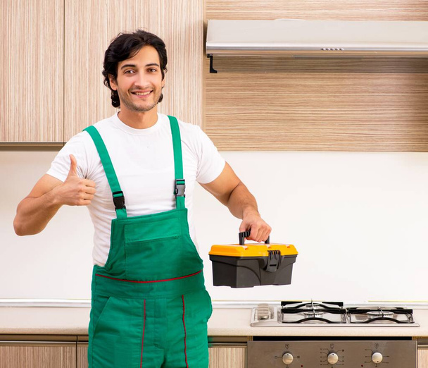 Der junge Bauunternehmer repariert den Ofen in der Küche - Foto, Bild
