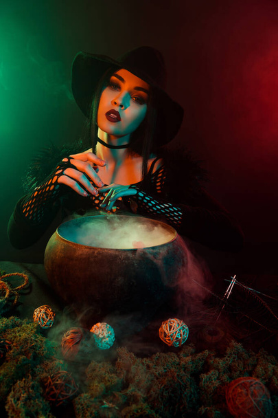 Photo of powerful witch doing magical ritual with cauldron potion summon demon devil over neon background. - Photo, Image