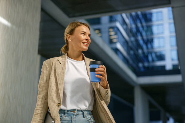 Positieve vrouwelijke manager die koffie drinkt tijdens de pauze in de buurt van kantoorgebouw. Hoge kwaliteit foto - Foto, afbeelding
