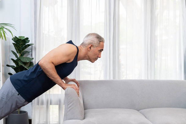 Sportowy i aktywny starszy mężczyzna za pomocą mebli do skutecznego kierowania mięśni z push up w domu ćwiczenia jako koncepcja zdrowego stylu życia po przejściu na emeryturę. Skutki - Zdjęcie, obraz