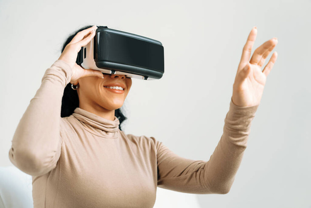 Jeune femme utilisant réalité virtuelle VR masque à la maison pour une expérience d'achat en ligne cruciale. L'innovation VR en réalité virtuelle optimisée pour le divertissement numérique féminin. - Photo, image
