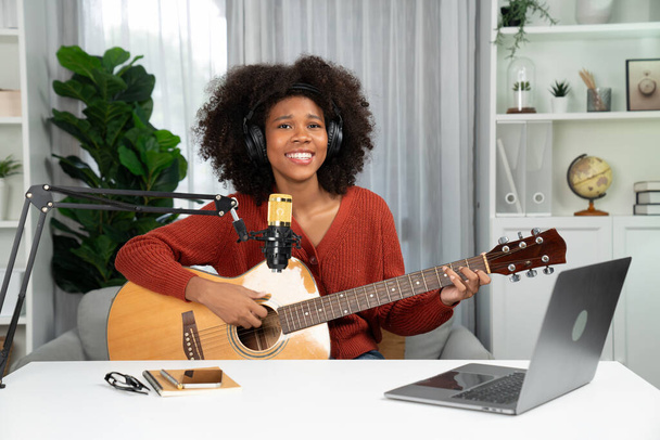 Canal anfitrião em músico de jovens afro-americanos tocando guitarra junto com o canto, transmitindo no laptop em estúdio. Decoração de equipamento de fones de ouvido e microfone de gravação. Gastemaker. - Foto, Imagem