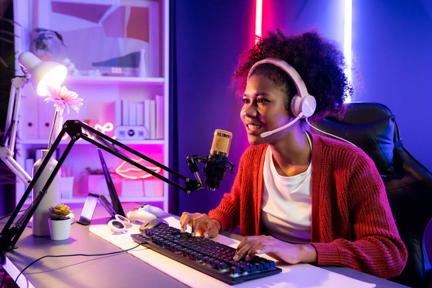 Afrikai amerikai lány streamer online játszik harcol Esport képzett csapat visel fejhallgató neon színű világítás szoba. Beszélgetni más játékosokkal stratégiákat tervez, hogy megnyerje a versenytársakat. Kóstoló. - Fotó, kép