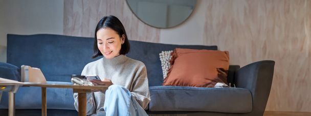 Technology and people. Young stylish asian woman sits at home with her smartphone, texting message, using application on mobile phone. - Foto, Imagem