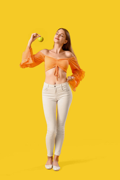 Hermosa joven con manzana fresca sobre fondo amarillo. Concepto de pérdida de peso - Foto, Imagen