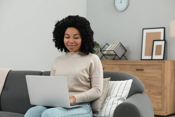Happy young woman using laptop on sofa indoors - Photo, image