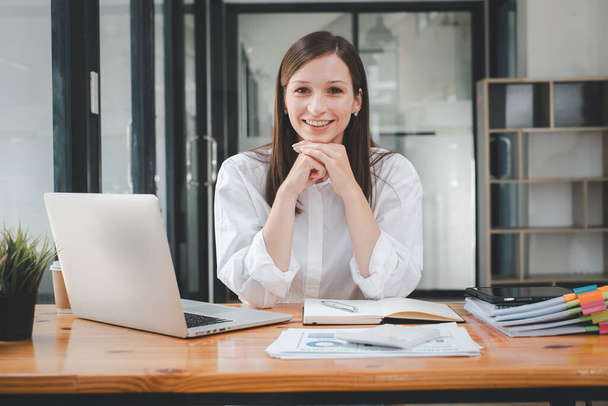 Portrait of young smiling woman looking at camera with crossed arms. Happy girl sitting in creative office. Successful businesswoman standing in office with copy space. - Photo, Image