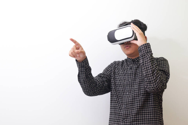 Retrato de un hombre asiático con camisa a cuadros negra usando gafas de Realidad Virtual (VR) y tratando de tocar algo frente a él. Imagen aislada sobre fondo blanco - Foto, imagen