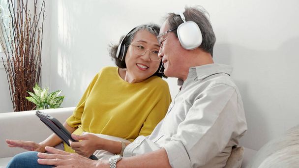 Geluk familie senior koppel het dragen van koptelefoon muziek luisteren en tablet kijken naar sociale media in de woonkamer thuis, gelukkig oudere man en vrouw ontspannen en gezellig met genieten, levensstijl concept. - Foto, afbeelding